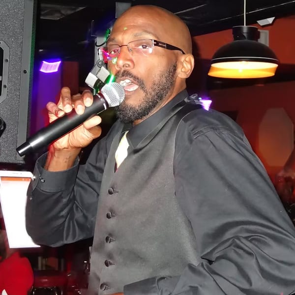 A man in a black shirt and vest sings into a microphone at Chicago Bar & Grill.