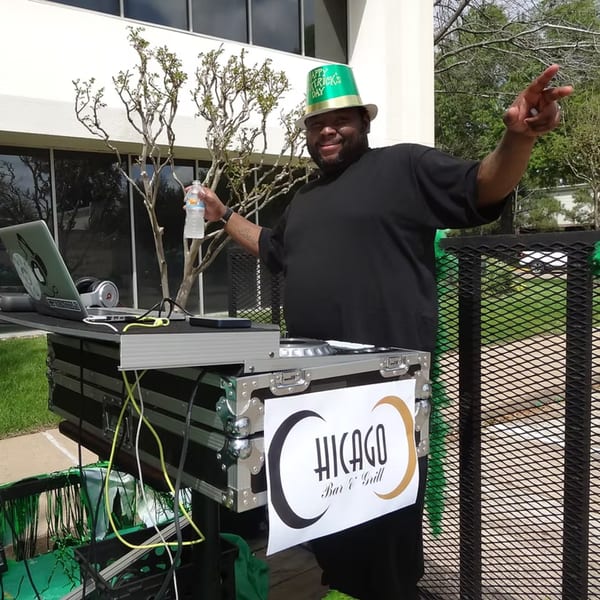 A DJ wearing a St. Patrick's Day hat, with a Chicago Bar & Grill sign on his equipment.