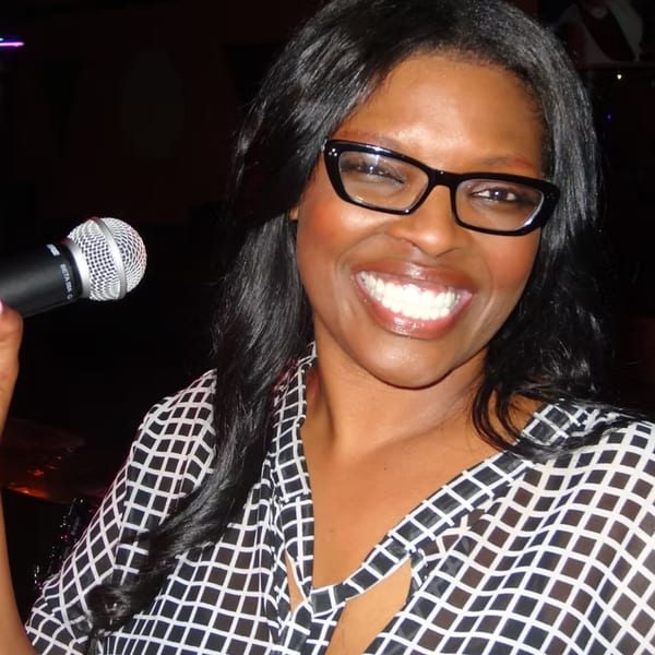 Smiling woman with long dark hair and glasses holding a microphone at Chicago Bar & Grill.