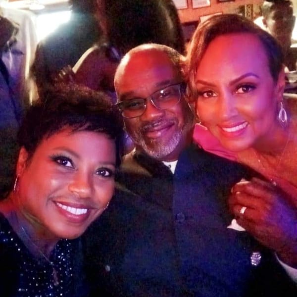 Three smiling people, two women and one man, posing closely together in a dimly lit bar.