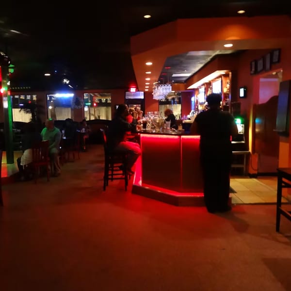 Dimly lit Chicago Bar & Grill interior with patrons at tables and a glowing red bar.