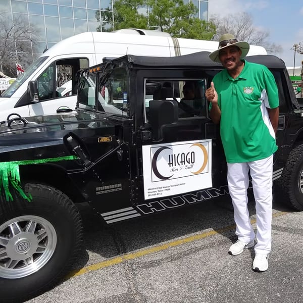 Man in a green shirt and hat stands next to a black Hummer with Chicago Bar & Grill branding.