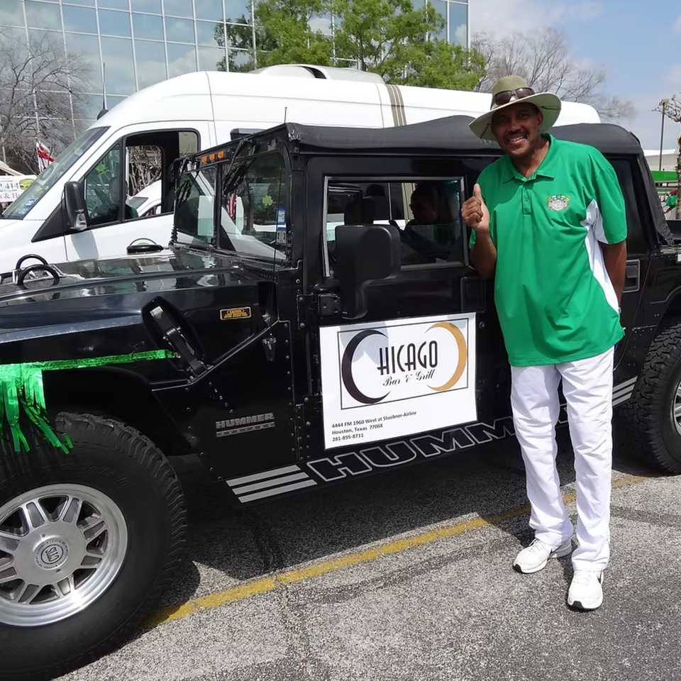Man in a green shirt and hat stands next to a black Hummer with Chicago Bar & Grill branding.