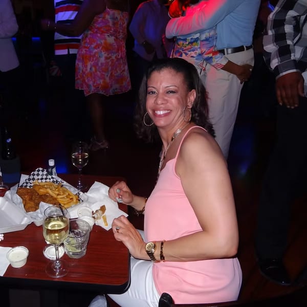 A smiling woman at Chicago Bar & Grill enjoys fish and chips with white wine.