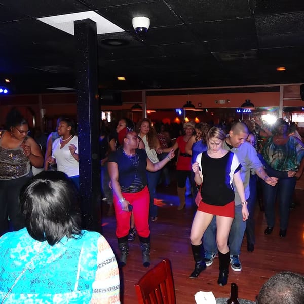 Patrons dancing on a wooden floor at Chicago Bar & Grill, with blue and red lighting.