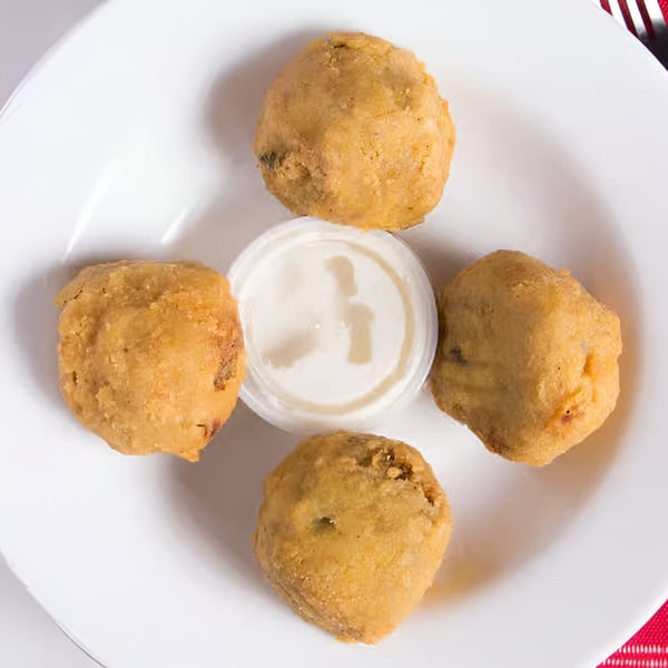 Four golden-brown fried mushrooms arranged around a small cup of white dipping sauce on a white plate.