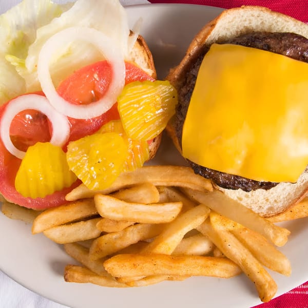 Open-faced cheeseburger with lettuce, tomato, onion, pickles, and a side of golden fries.