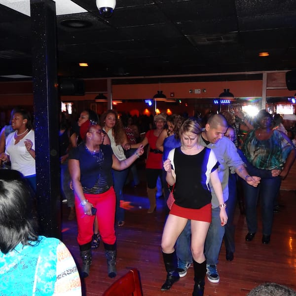 People dancing on a wooden floor in a dimly lit club with blue and red lighting.